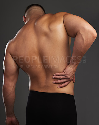 Buy stock photo Cropped shot of an unrecognizable and athletic young man holding his back in pain while shirtless in studio against a dark background