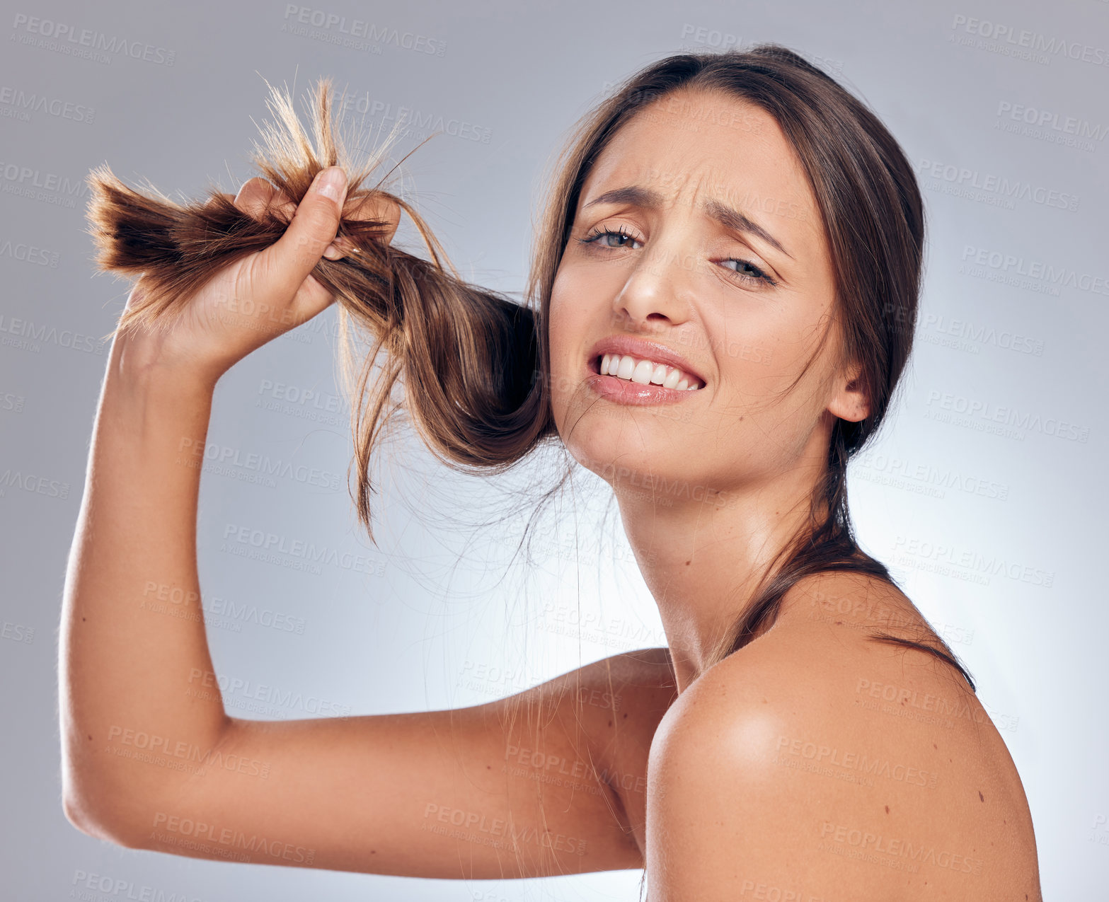 Buy stock photo Shot of an attractive young woman standing alone in the studio and looking upset while holding her hair