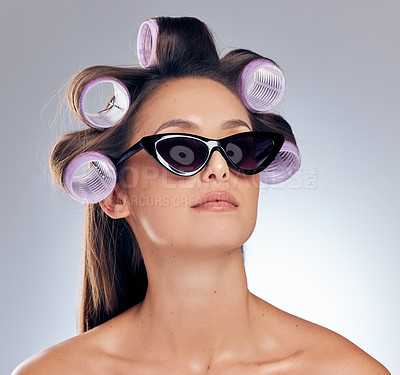 Buy stock photo Shot of an attractive young woman standing alone in the studio with rollers in her hair and wearing with sunglasses