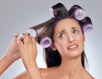 Buy stock photo Shot of a young woman standing in the studio and feeling stressed while trying to put rollers in her hair