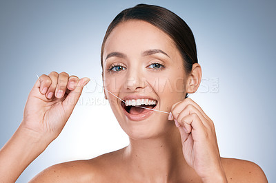 Buy stock photo Portrait of a young beautiful woman flossing her teeth against a blue background