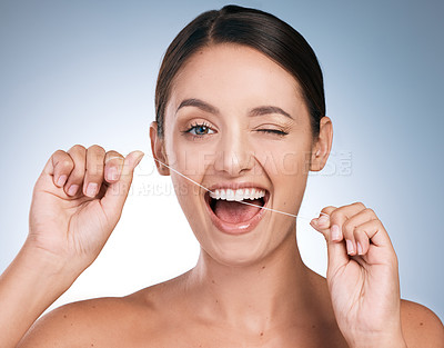 Buy stock photo Portrait of a young beautiful woman flossing her teeth against a blue background