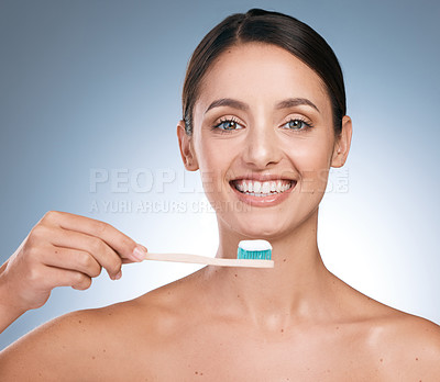 Buy stock photo Portrait of a young beautiful woman brushing her teeth against a blue background