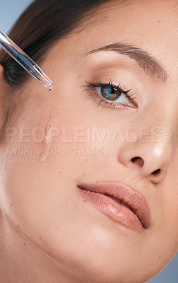 Buy stock photo Cropped shot of a young beautiful woman applying serum to her face against a blue background