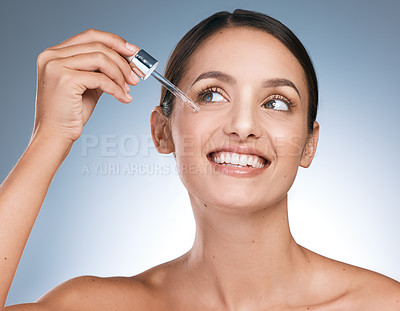 Buy stock photo Shot of a young beautiful woman applying serum to her face against a blue background
