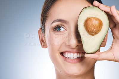 Buy stock photo Shot of an attractive young woman posing with a sliced avocado against a blue background