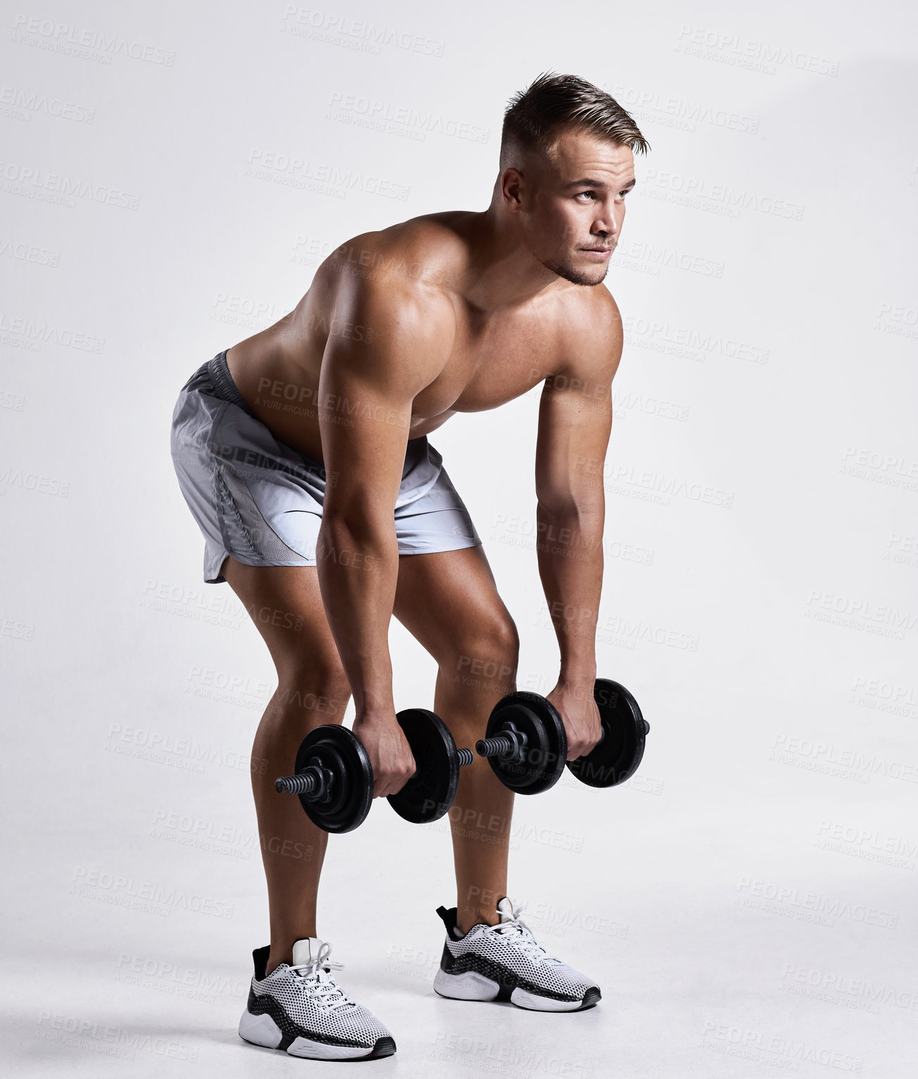 Buy stock photo Shot of a sporty young man working out with dumbbells against a grey background