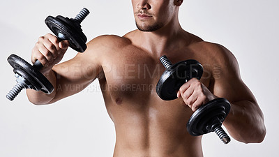 Buy stock photo Shot of a sporty young man working out with dumbbells against a grey background