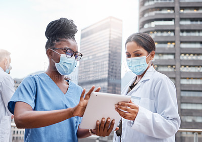 Buy stock photo Shot of two young female doctors using a digital tablet in the city