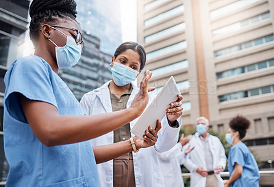 Buy stock photo Shot of two young female doctors using a digital tablet in the city