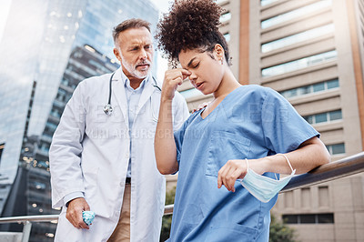 Buy stock photo Shot of a young female nurse suffering from a headache while talking to a colleague in the city