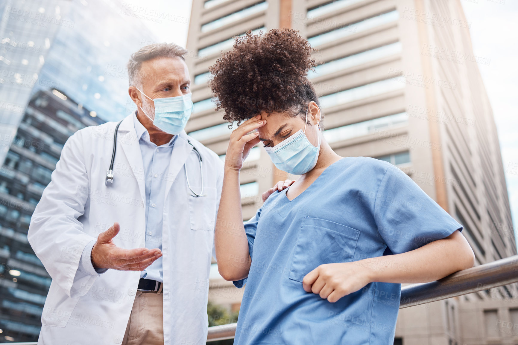 Buy stock photo Shot of a young female nurse suffering from a headache while talking to a colleague in the city