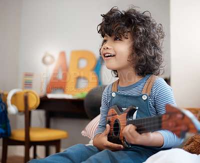 Buy stock photo Shot of an adorable young boy playing with a guitar in his bedroom at home