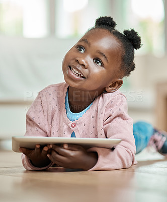 Buy stock photo Full length shot of an adorable little girl using a tablet while lying on the living room floor at home