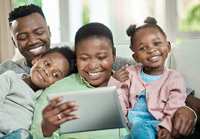 Buy stock photo Cropped shot of an affectionate young family of four using a tablet while sitting on a sofa in their living room at home