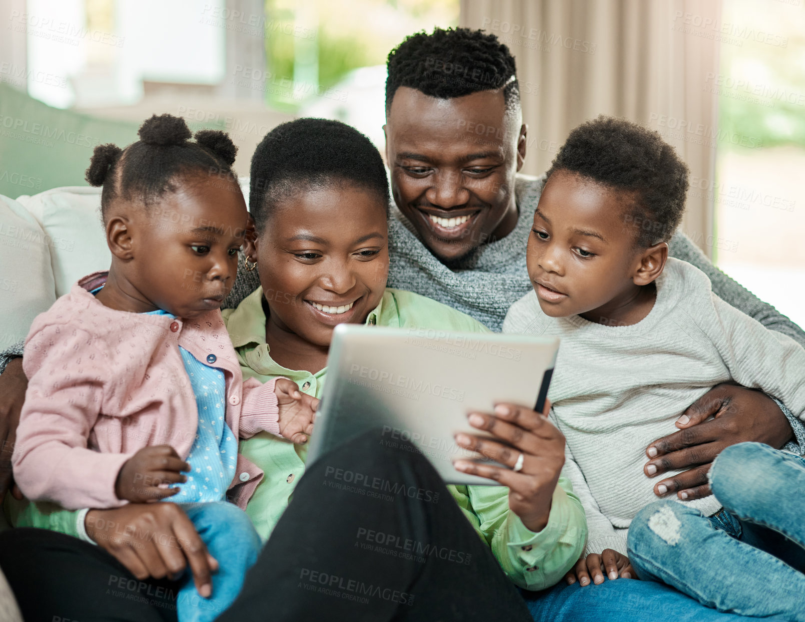 Buy stock photo Cropped shot of an affectionate young family of four using a tablet while sitting on a sofa in their living room at home