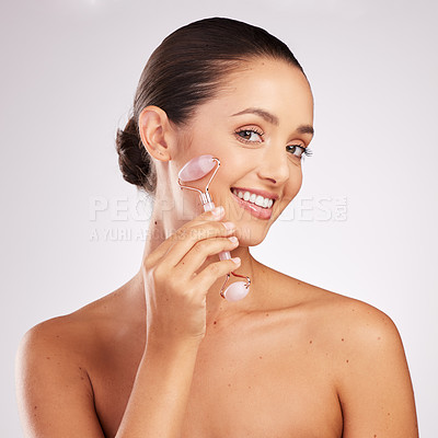 Buy stock photo Shot of an attractive young woman using a jade roller on her face against a studio background