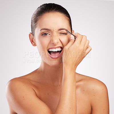 Buy stock photo Shot of an attractive young woman plucking her eyebrows against a studio background