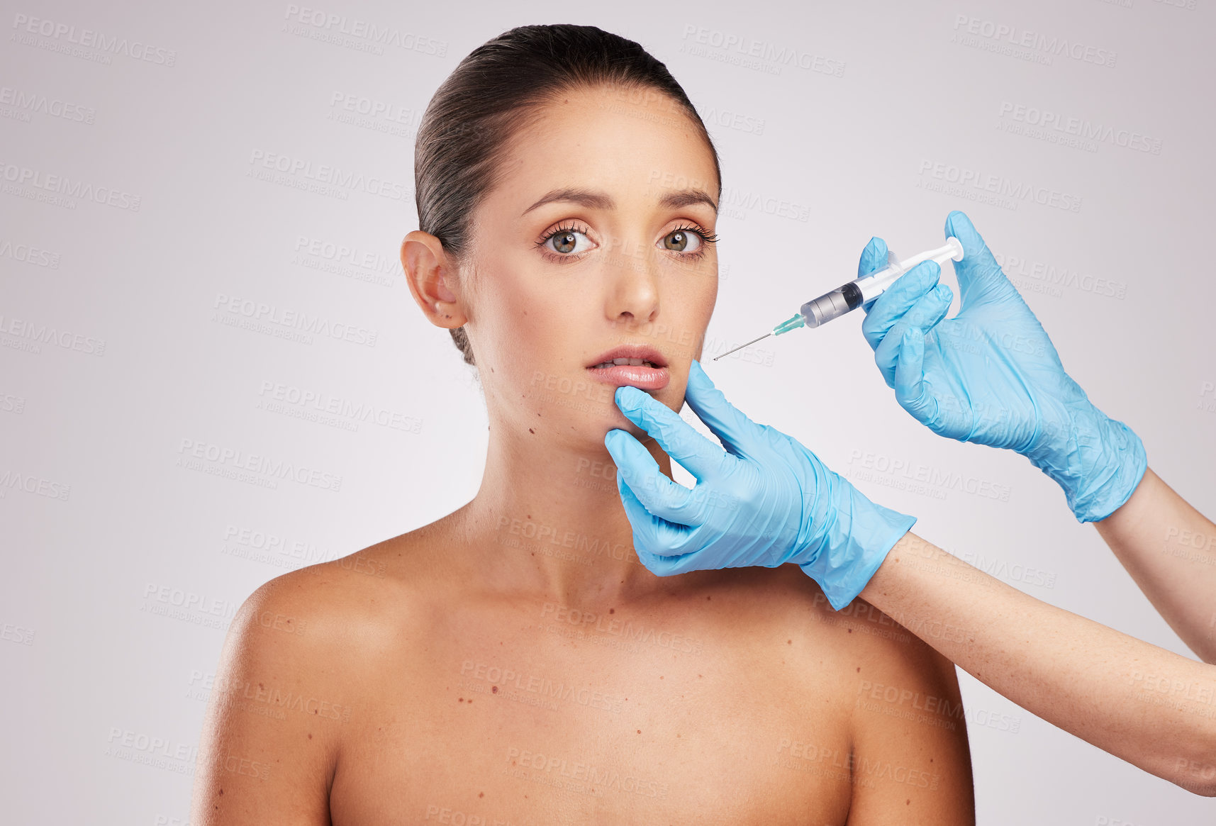 Buy stock photo Shot of an attractive young woman getting her face injected by gloved hands against a studio background
