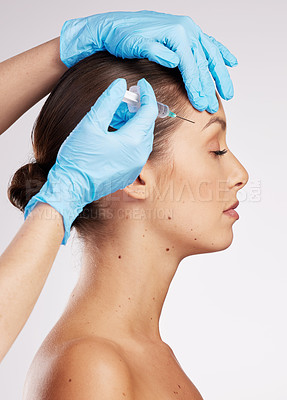 Buy stock photo Shot of an attractive young woman getting her face injected by gloved hands against a studio background
