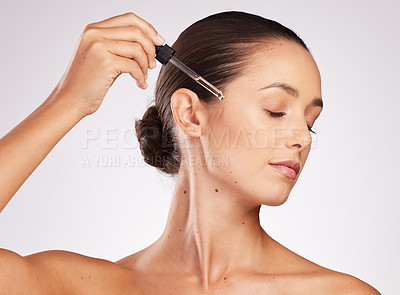Buy stock photo Shot of an attractive young woman using a serum on her face against a studio background