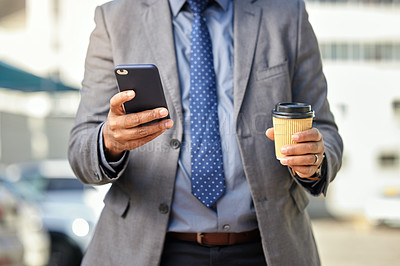 Buy stock photo Shot of a businessman holding his cellphone and a takeaway coffee while out in the city
