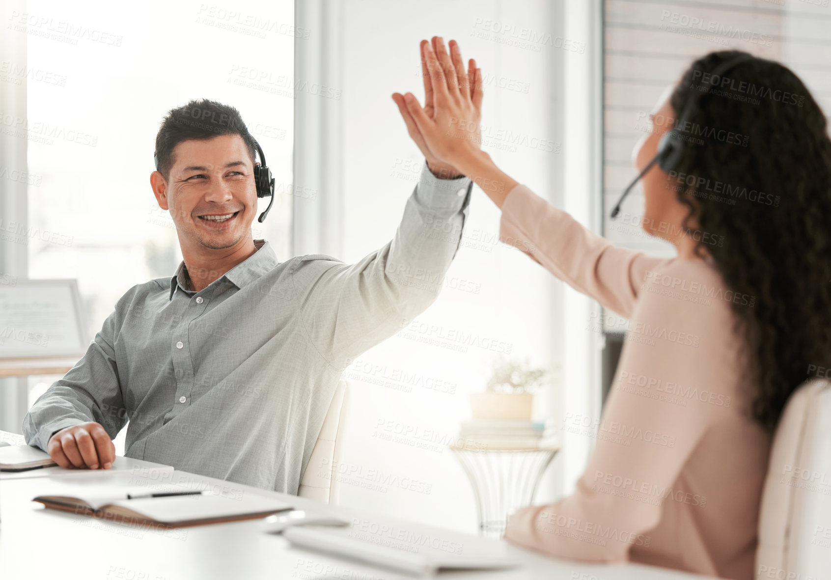 Buy stock photo Shot of two young call center agents giving each other a high five in an office at work