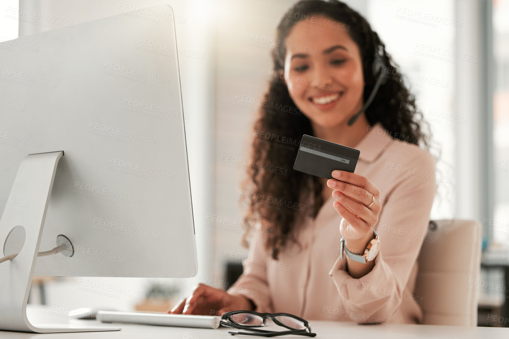 Buy stock photo Shot of a young female call center agent using a credit card at work