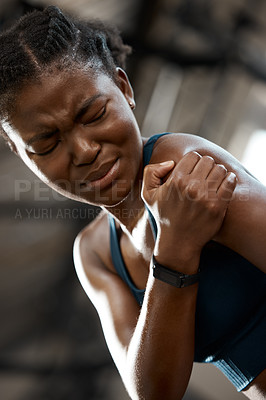 Buy stock photo Low angle shot of an attractive and athletic young woman holding her shoulder in pain while at the gym