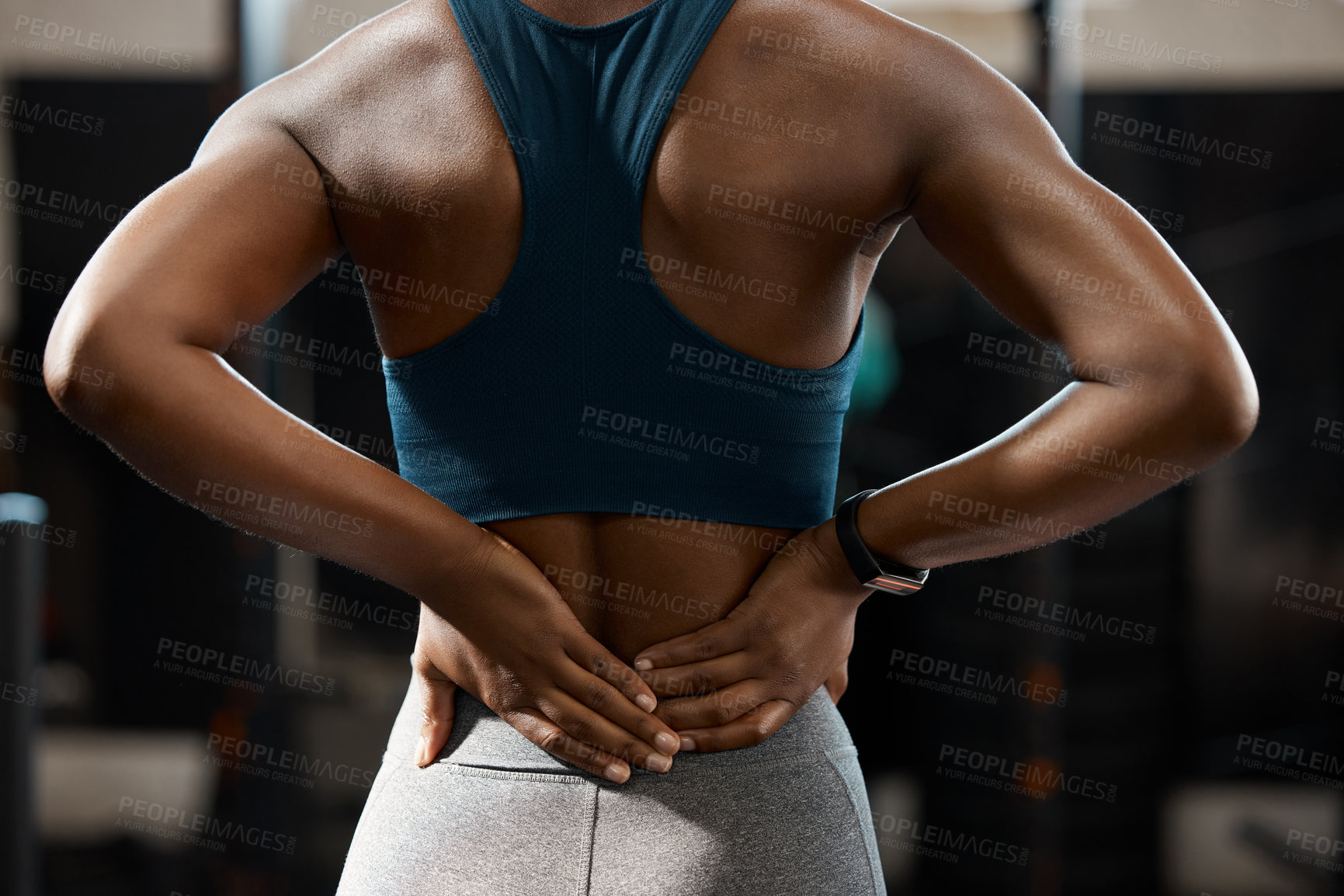 Buy stock photo Rearview shot of an unrecognizable and athletic young woman holding her lower back in pain while at the gym