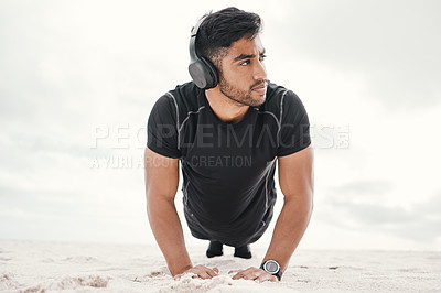 Buy stock photo Shot of a sporty young man wearing headphones while doing push ups on the beach