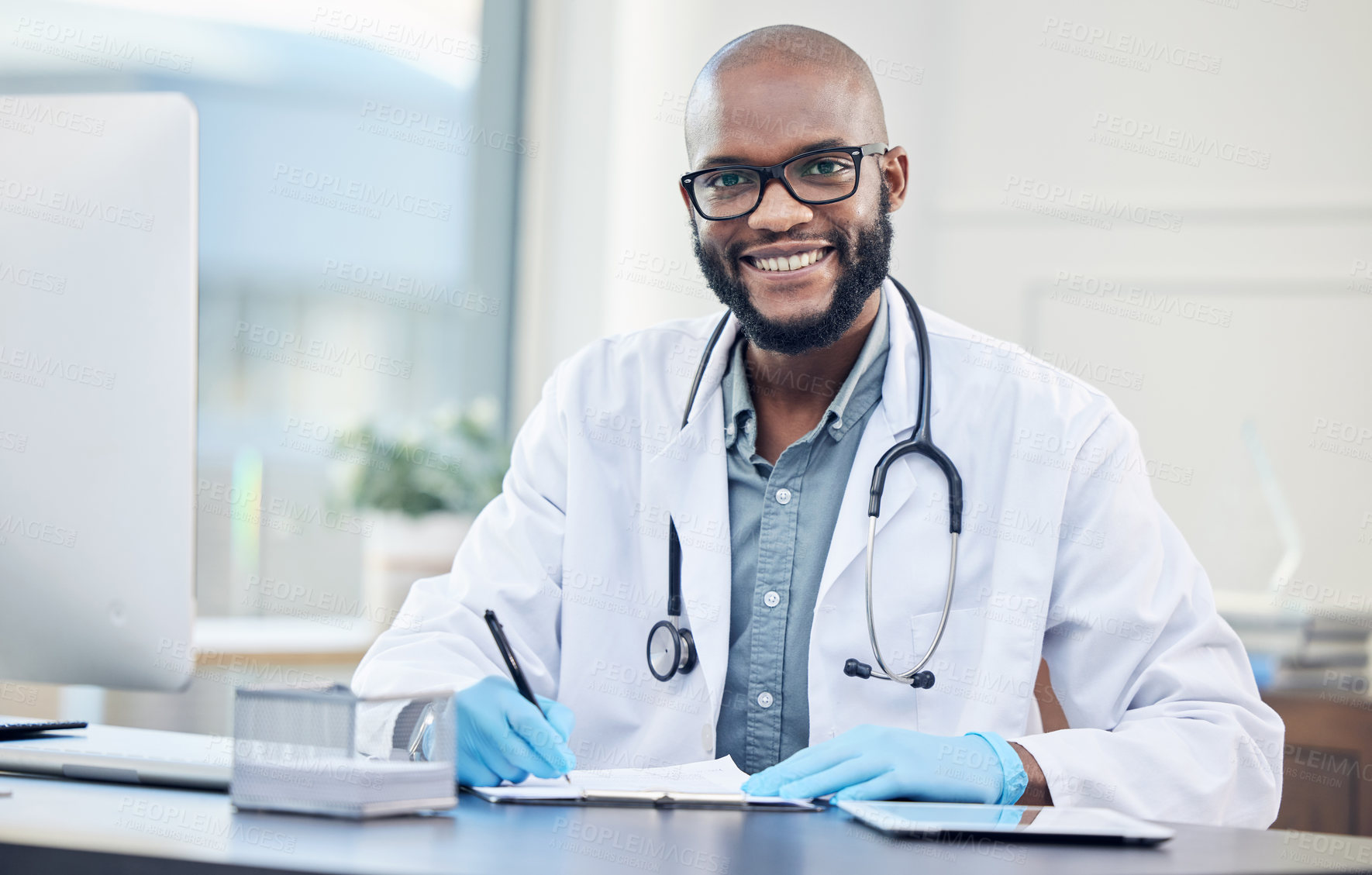 Buy stock photo Shot of a handsome young doctor sitting alone in his clinic and making notes