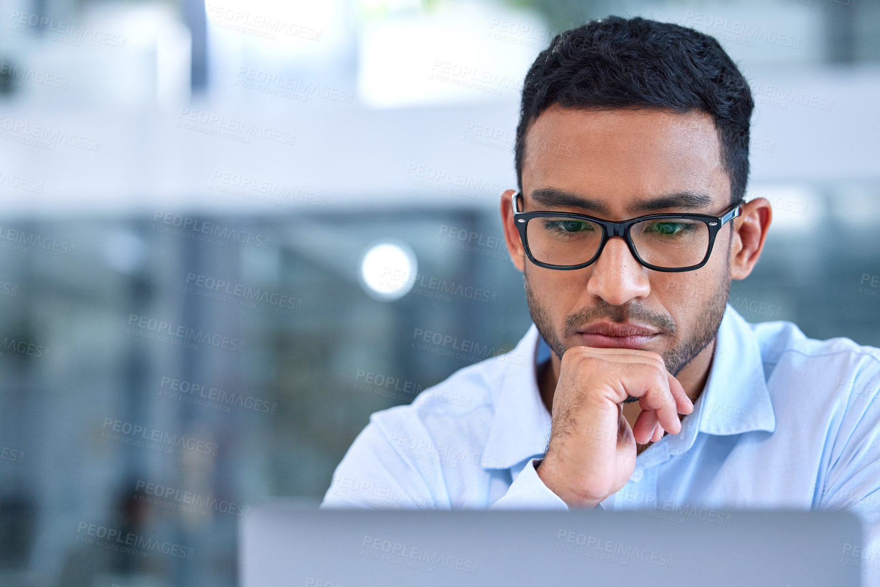 Buy stock photo Shot of a young businessman using his laptop at work