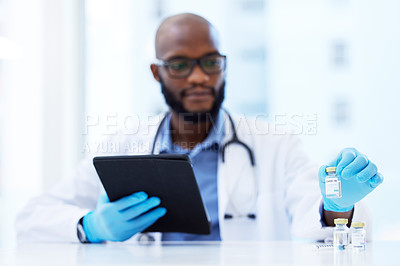 Buy stock photo Shot of a young doctor sitting in his clinic and using a digital tablet while checking Covid-19 vaccine vials