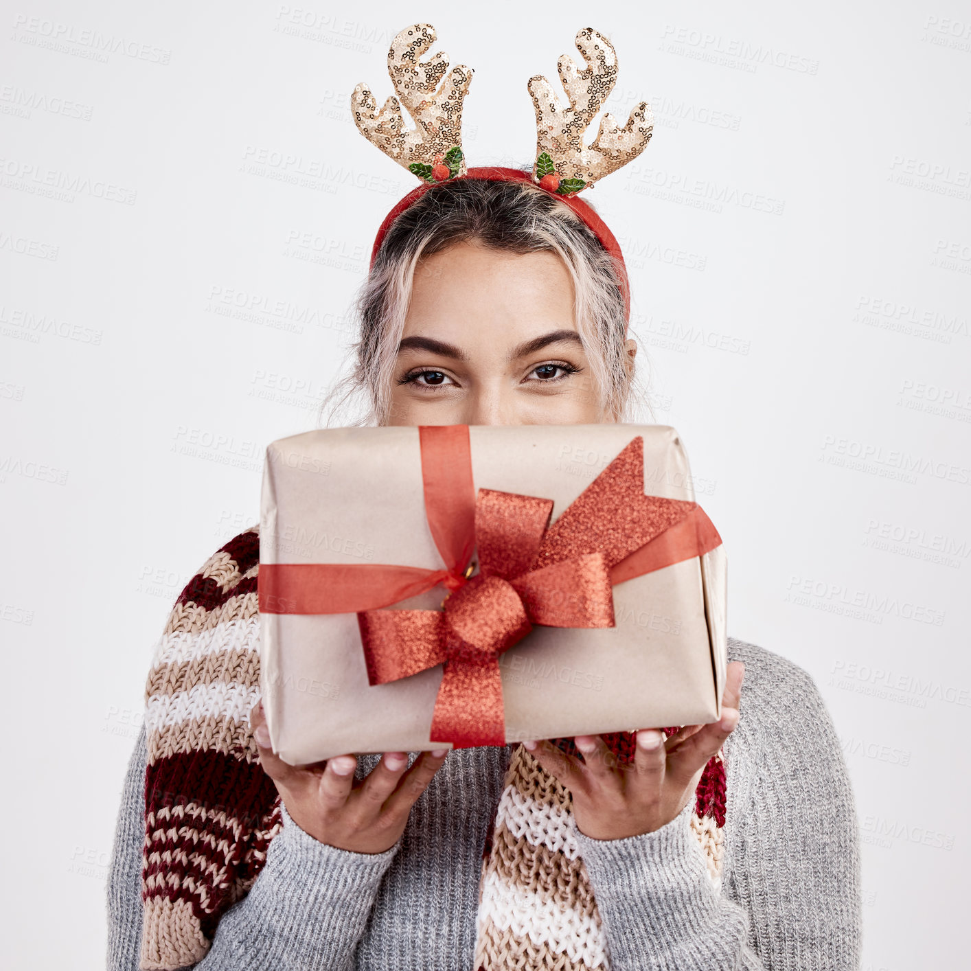 Buy stock photo Studio portrait of an attractive young woman holding a present up in front of her face while dressed in Christmas-themed attire