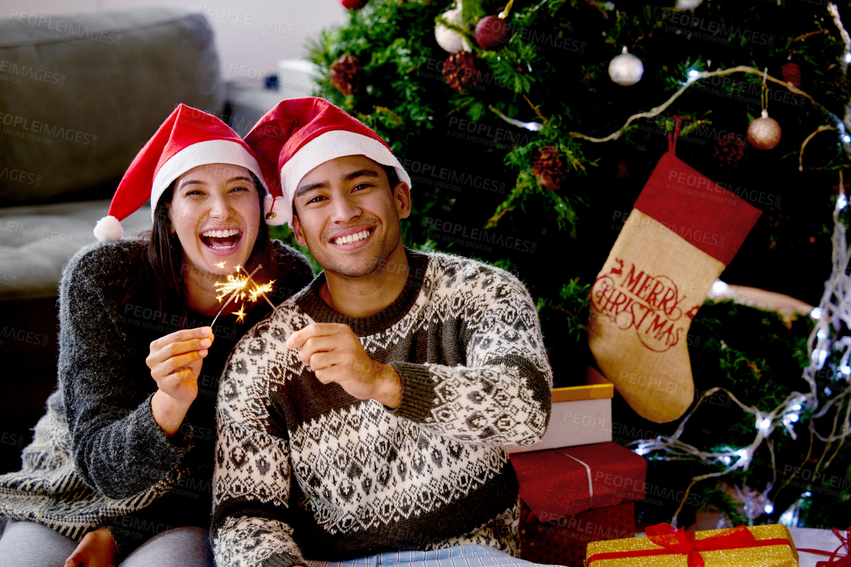 Buy stock photo Shot of a young couple sitting by their Christmas tree