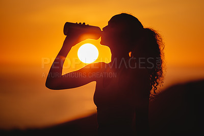 Buy stock photo Cropped shot of an unrecognizable and athletic young woman drinking water while exercising outside at sunset