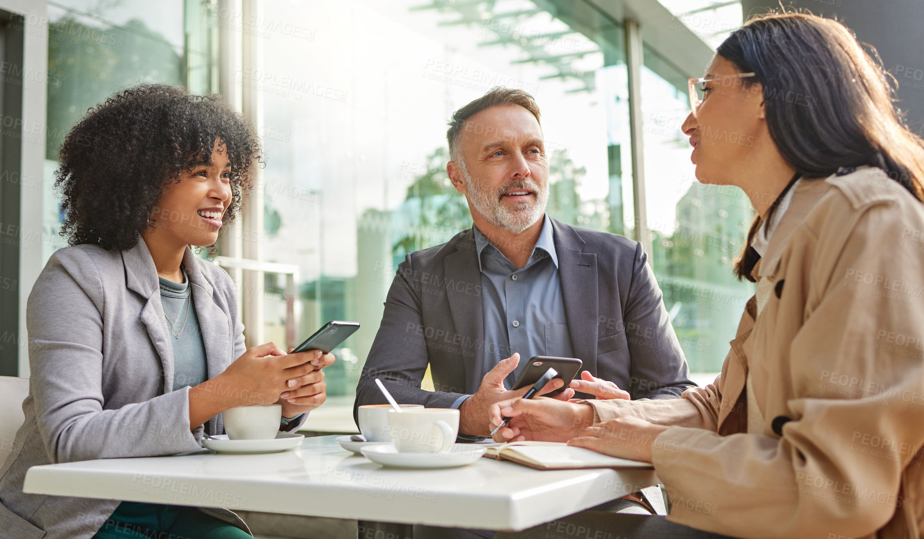 Buy stock photo Shot of a group of colleagues brainstorming ideas at a coffee shop while using their smartphones