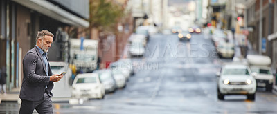 Buy stock photo Shot of a handsome businessman walking through the city while using his smartphone