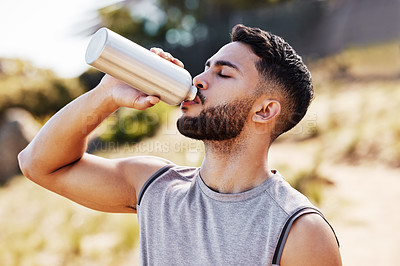 Buy stock photo Shot of a handsome young man standing alone outside and drinking water during his run