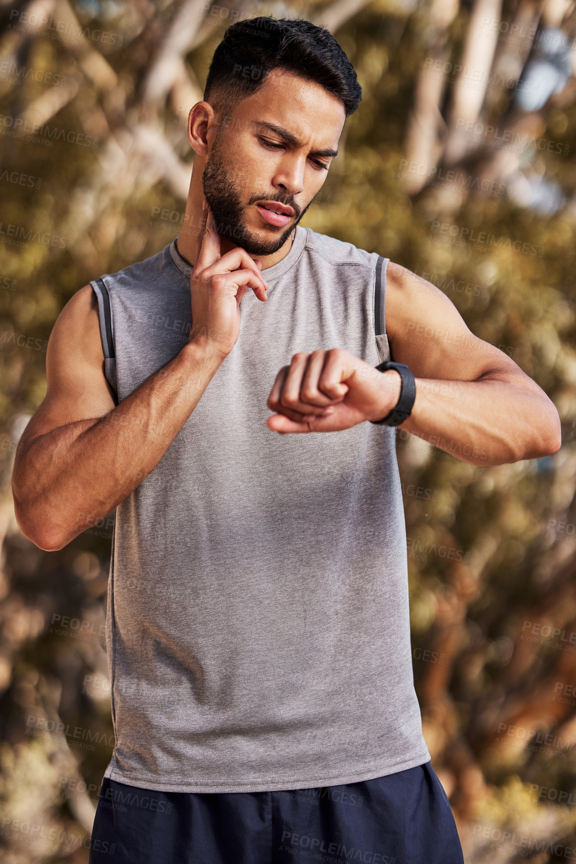 Buy stock photo Shot of a handsome young man standing alone outside and using his watch to time his pulse after a run