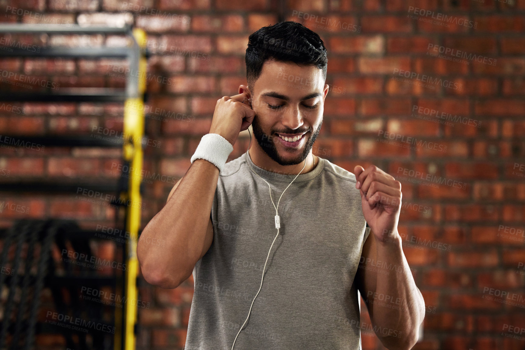 Buy stock photo Shot of a young man stretching using earphones during his workout in the gym