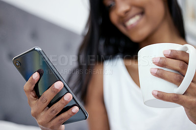 Buy stock photo Shot of a woman holding her cellphone and a cup of coffee while sitting at home