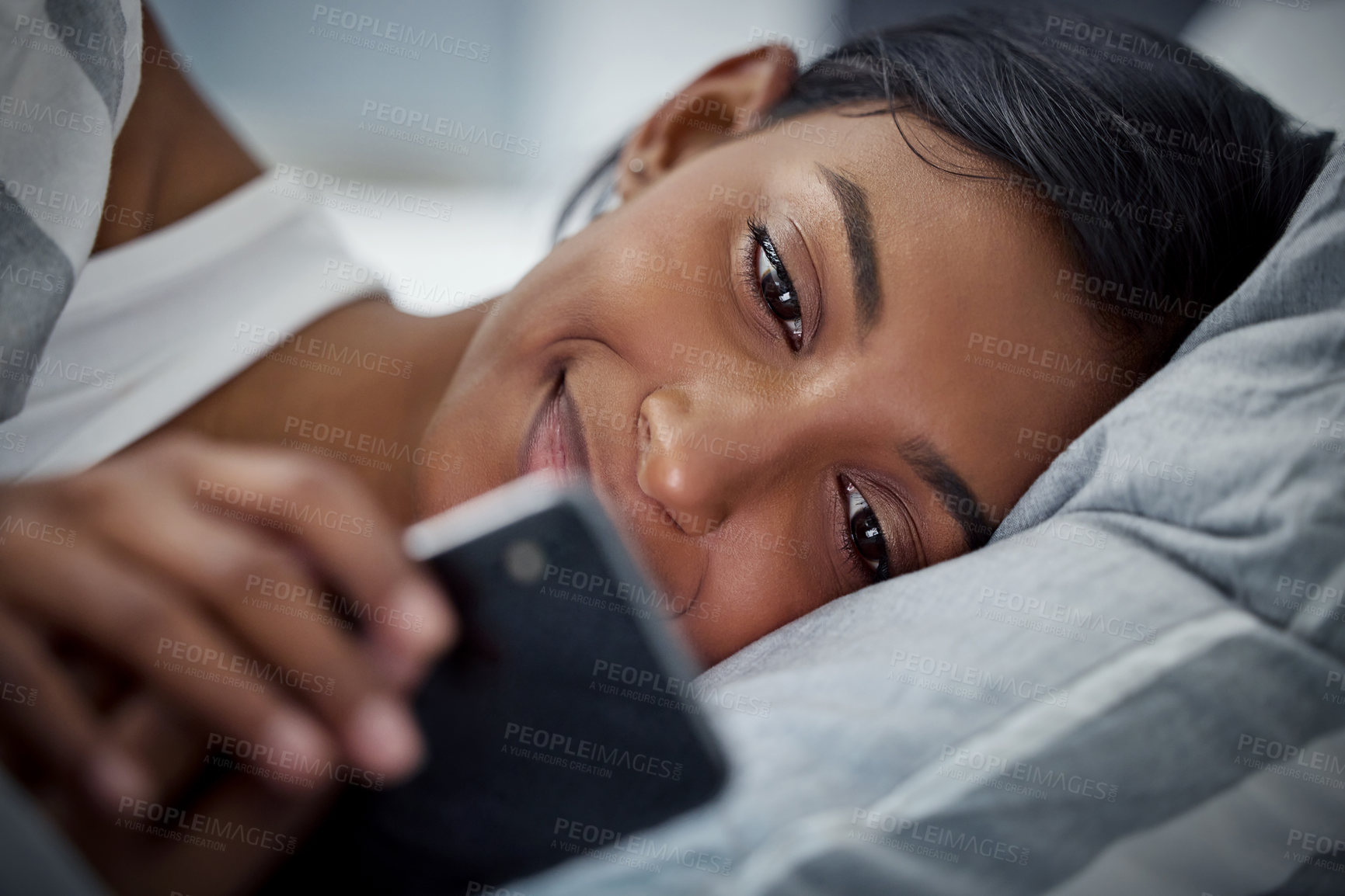 Buy stock photo Shot of a beautiful young woman using her cellphone while lying in her bed