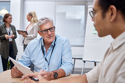Buy stock photo Shot of a mature businessman sitting with a colleague and having a discussion while going through paperwork