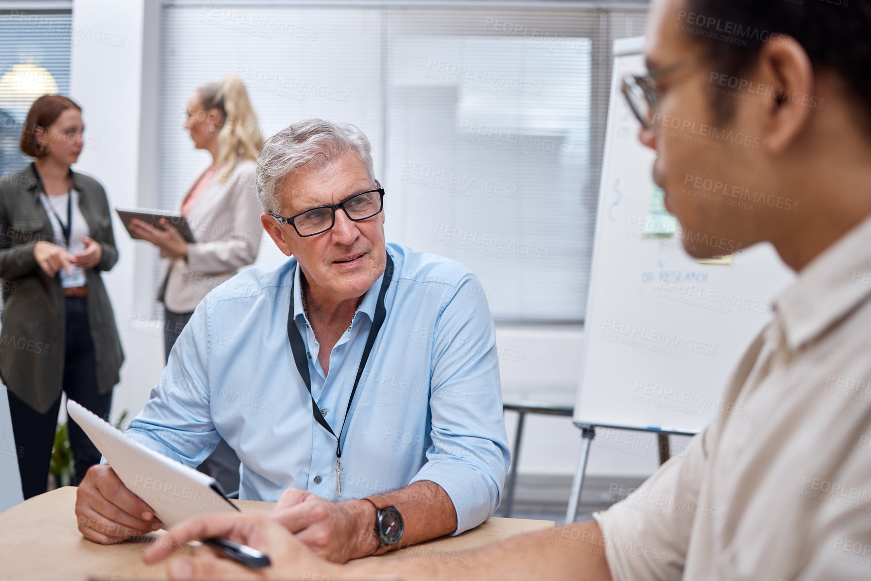 Buy stock photo Shot of a mature businessman sitting with a colleague and having a discussion while going through paperwork