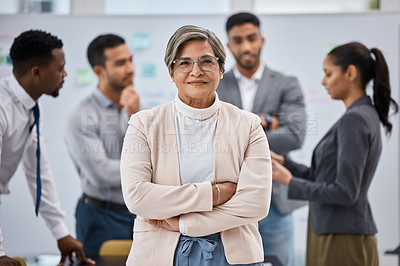 Buy stock photo Portrait of a mature businesswoman standing with her arms crossed in an office with her colleagues in the background