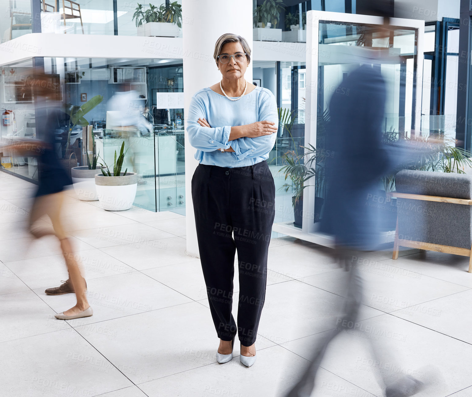 Buy stock photo Portrait of a mature businesswoman standing with her arms crossed in a busy office