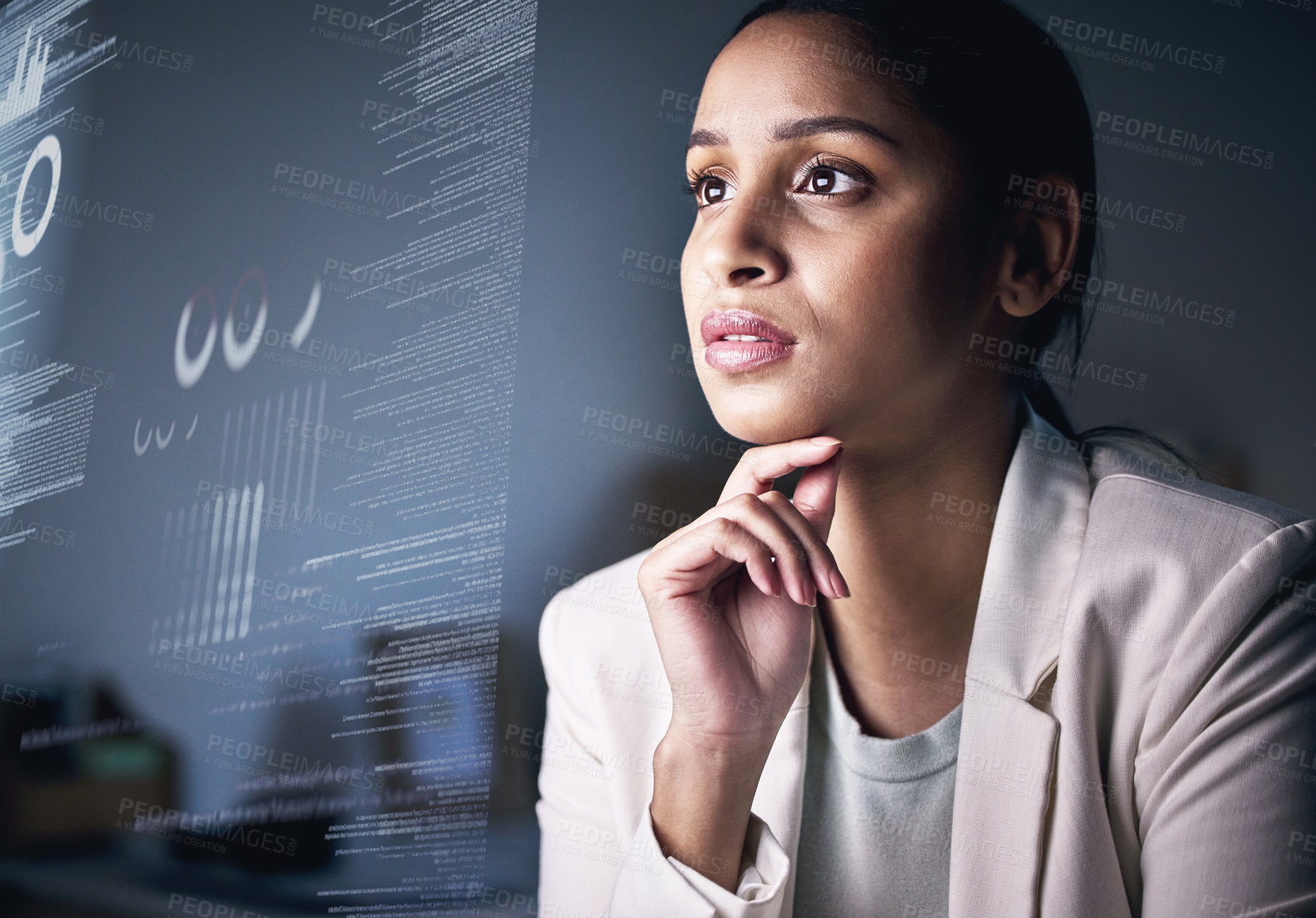 Buy stock photo Shot of an attractive young businesswoman sitting alone in the office at night and looking contemplative while using her computer