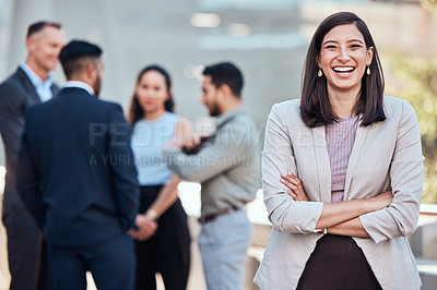 Buy stock photo Shot of an attractive young businesswoman standing outside with her arms folded while her colleagues stand behind her